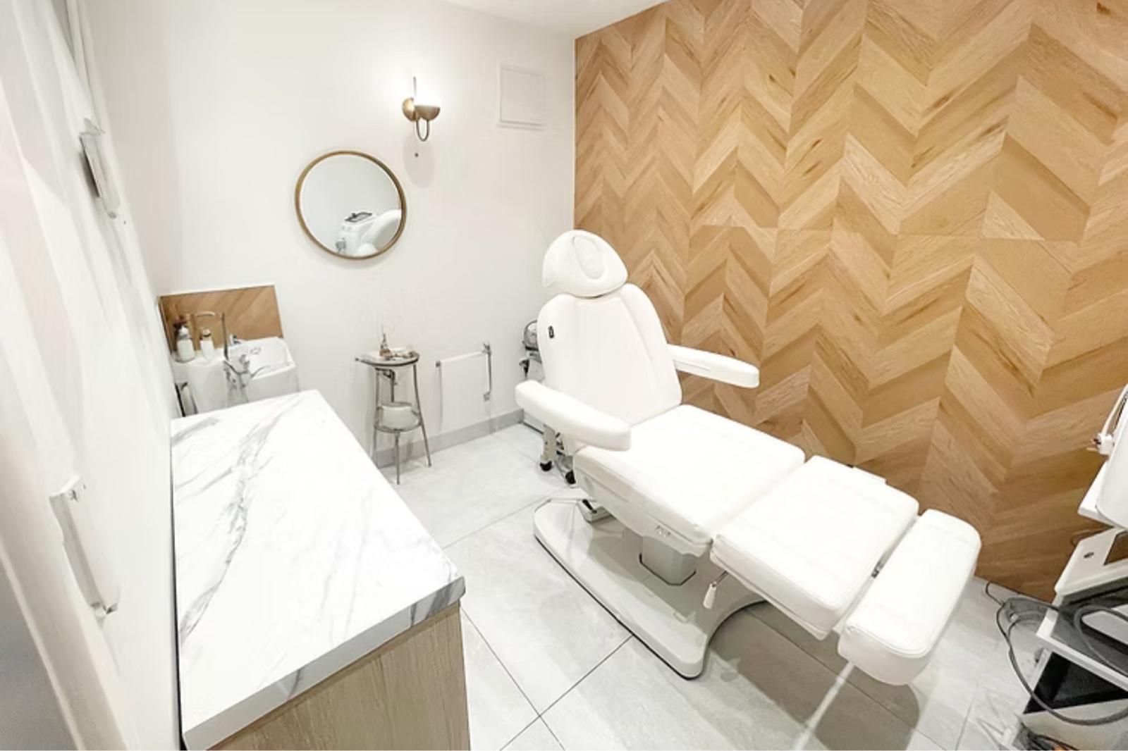 The treatment room: a white reclining treatment chair against a herringbone oak wall, with a marble counter and basin.